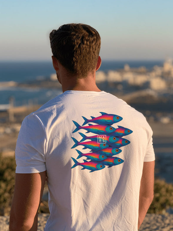 Homme au bord de mer portant un tee shirt avec une illustration de sardines dans le dos