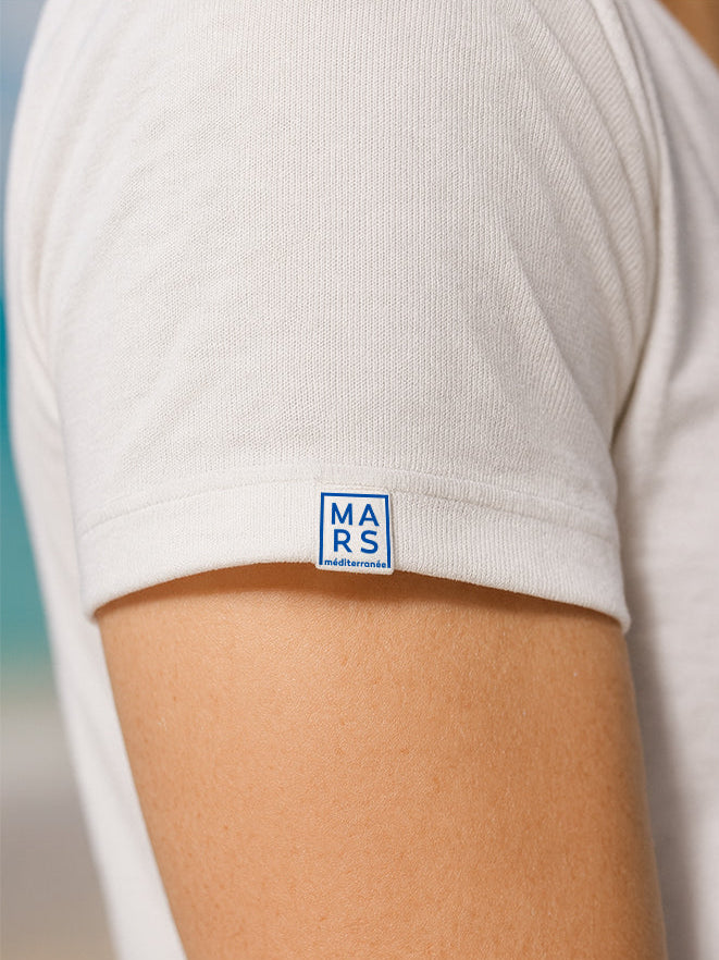 Une manche d’un t-shirt blanc avec dessus une etiquette en bleue 