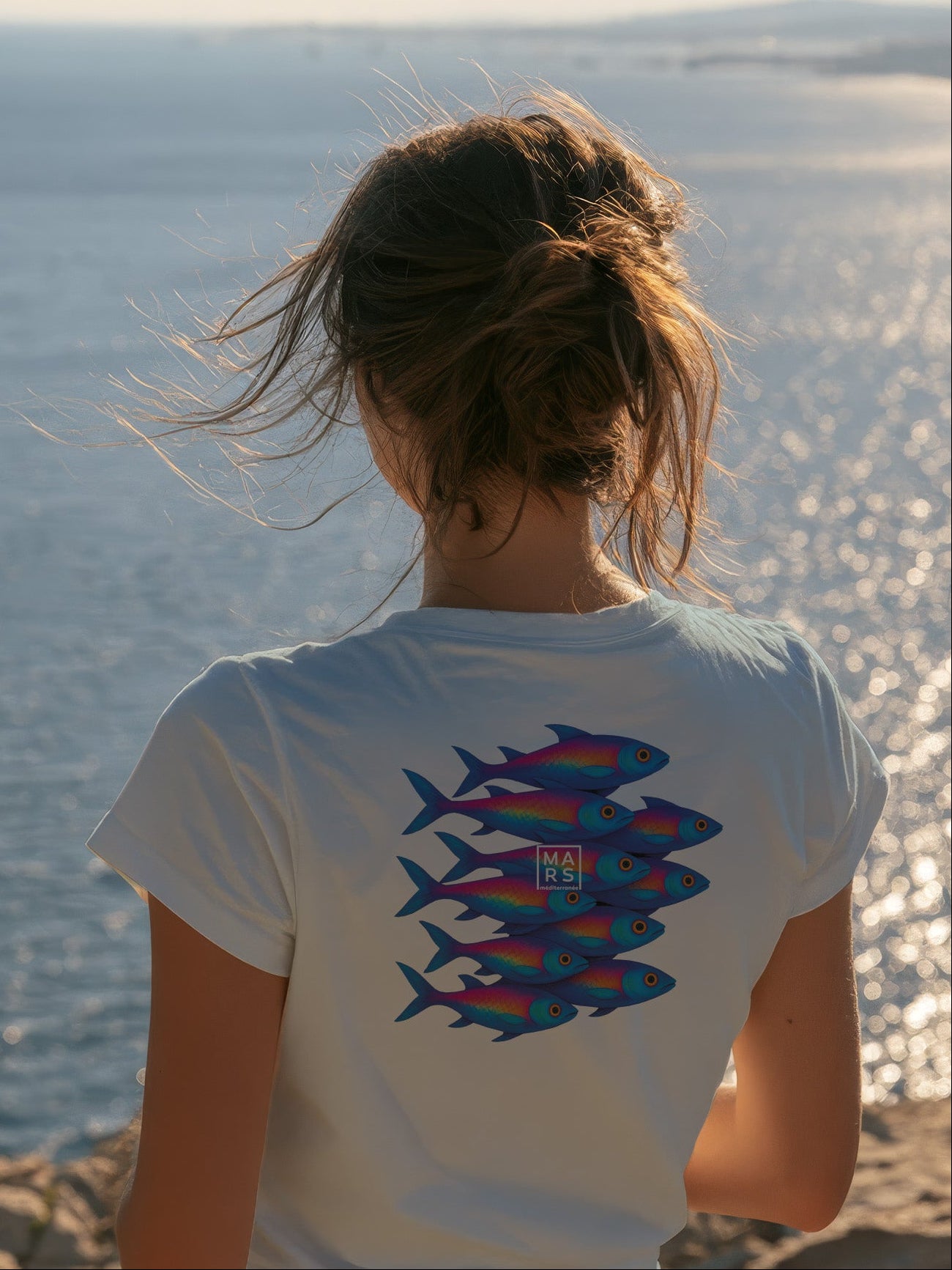 Femme au bord de mer portant un tee-shirt bleu avec une illustration de sardines