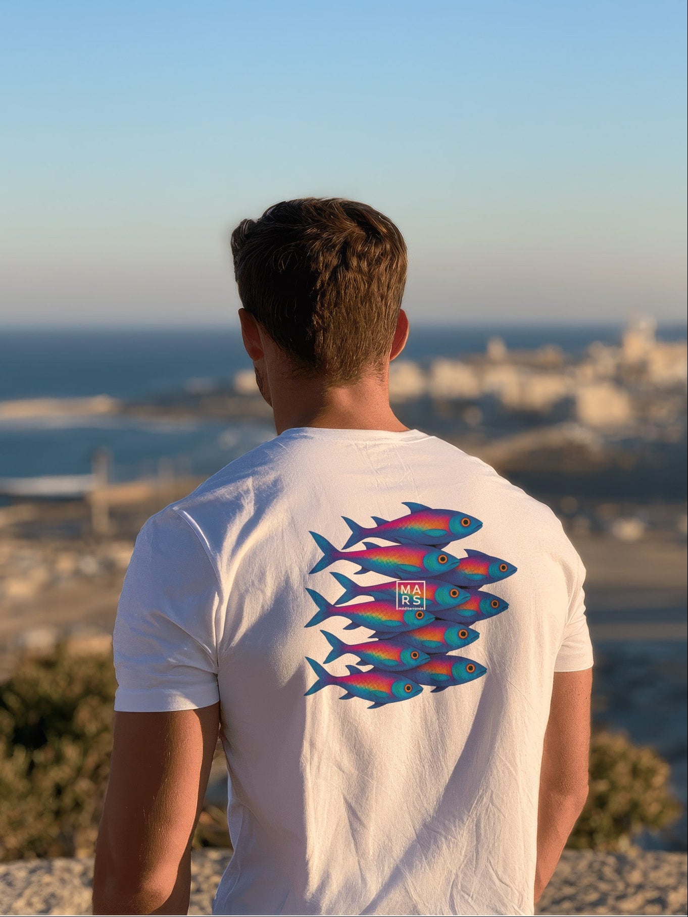 Homme au bord de mer portant un tee-shirt blanc et une illustration de sardines
