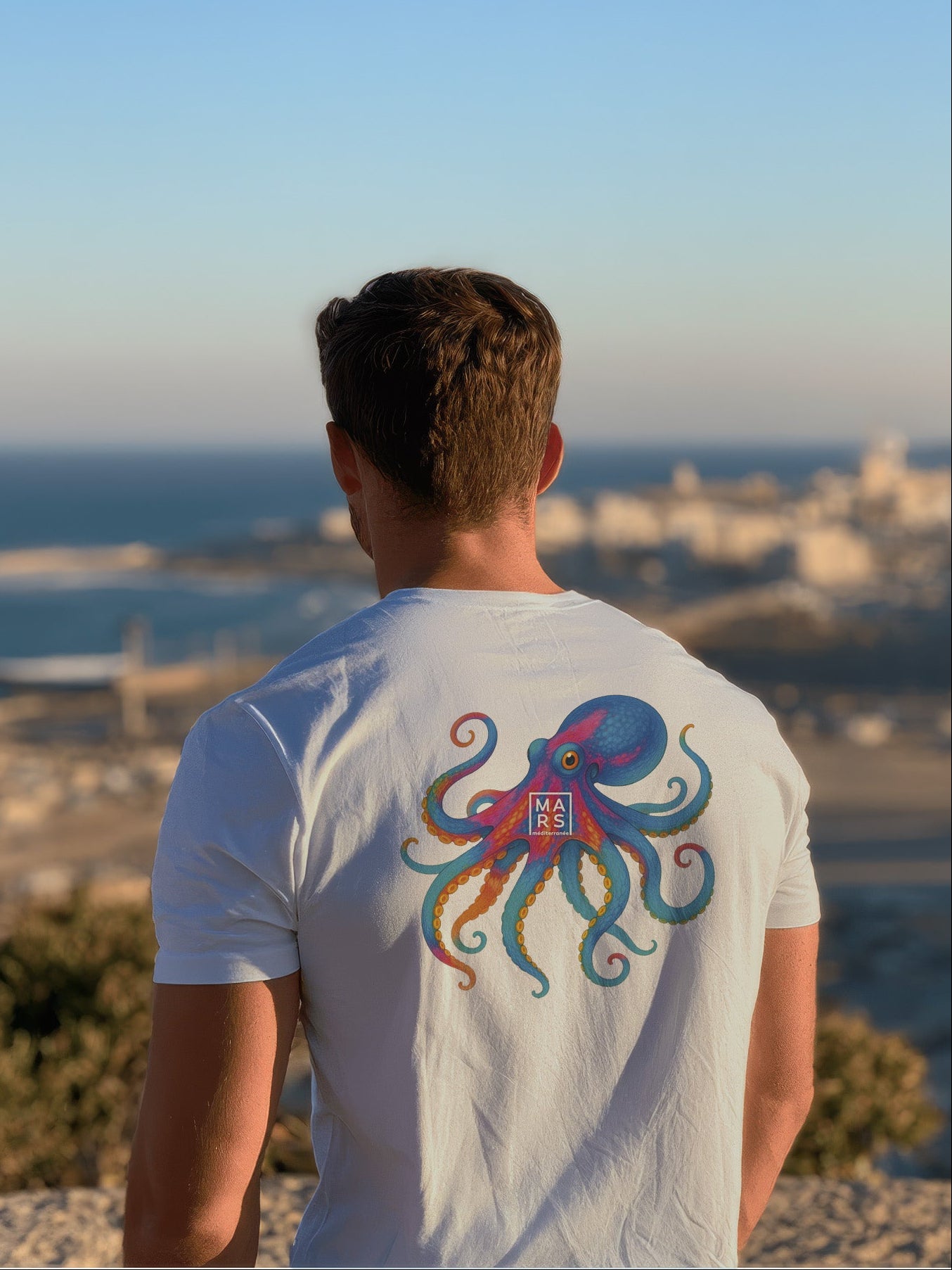Homme au bord de mer portant un tee-shirt bleu avec une illustration de poulpes