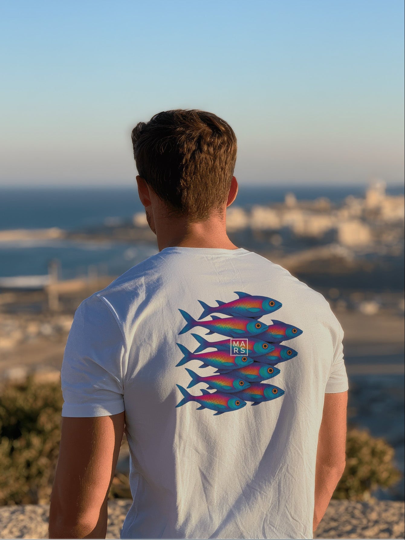Homme au bord de mer portant un tee-shirt bleu avec une illustration de sardines