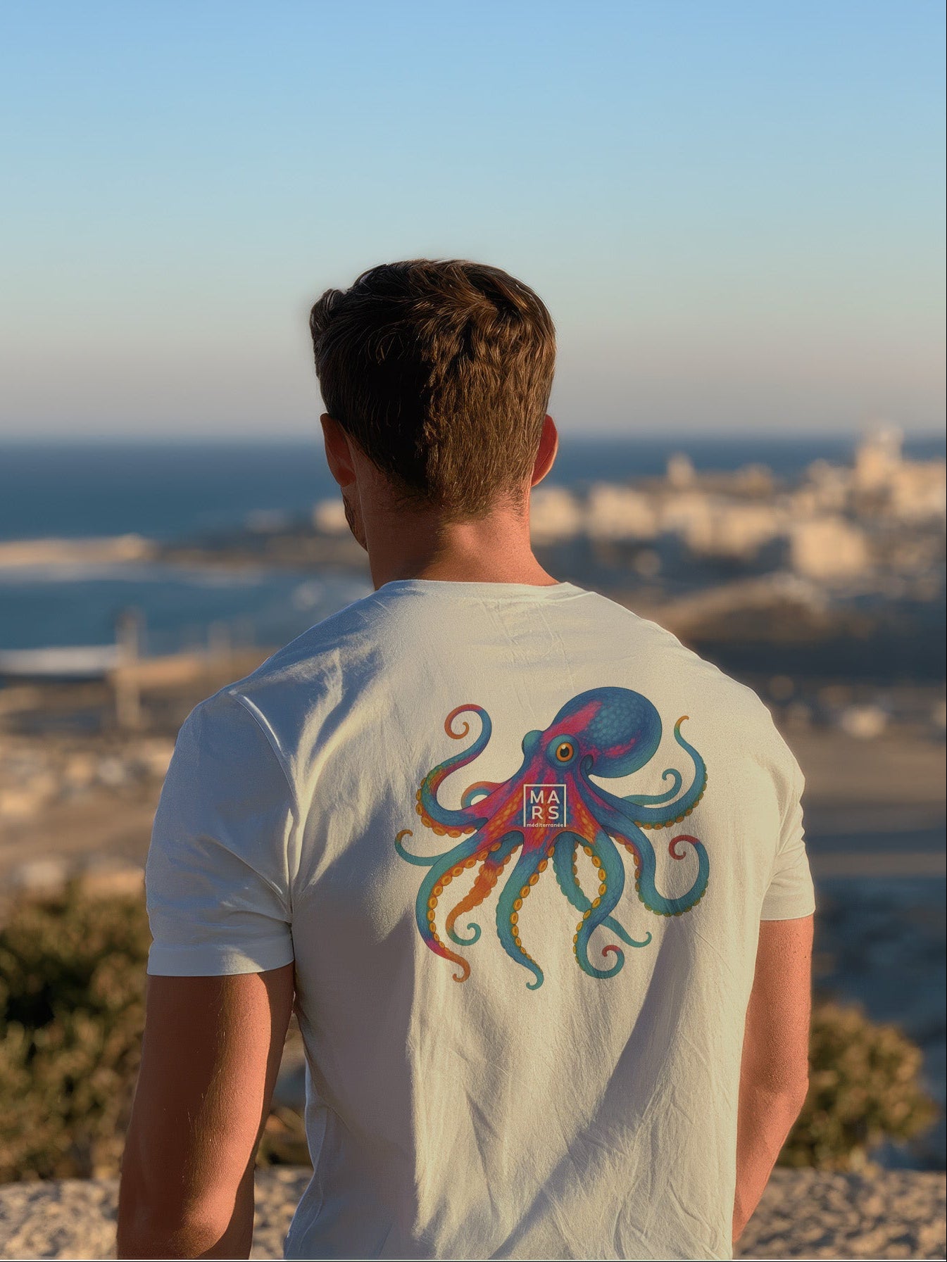 Homme au bord de mer portant un tee-shirt vert avec une illustration de poulpe