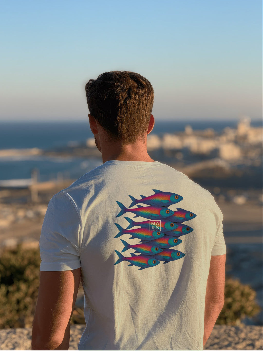 Homme au bord de mer portant un tee-shirt vert avec une illustration de sardines