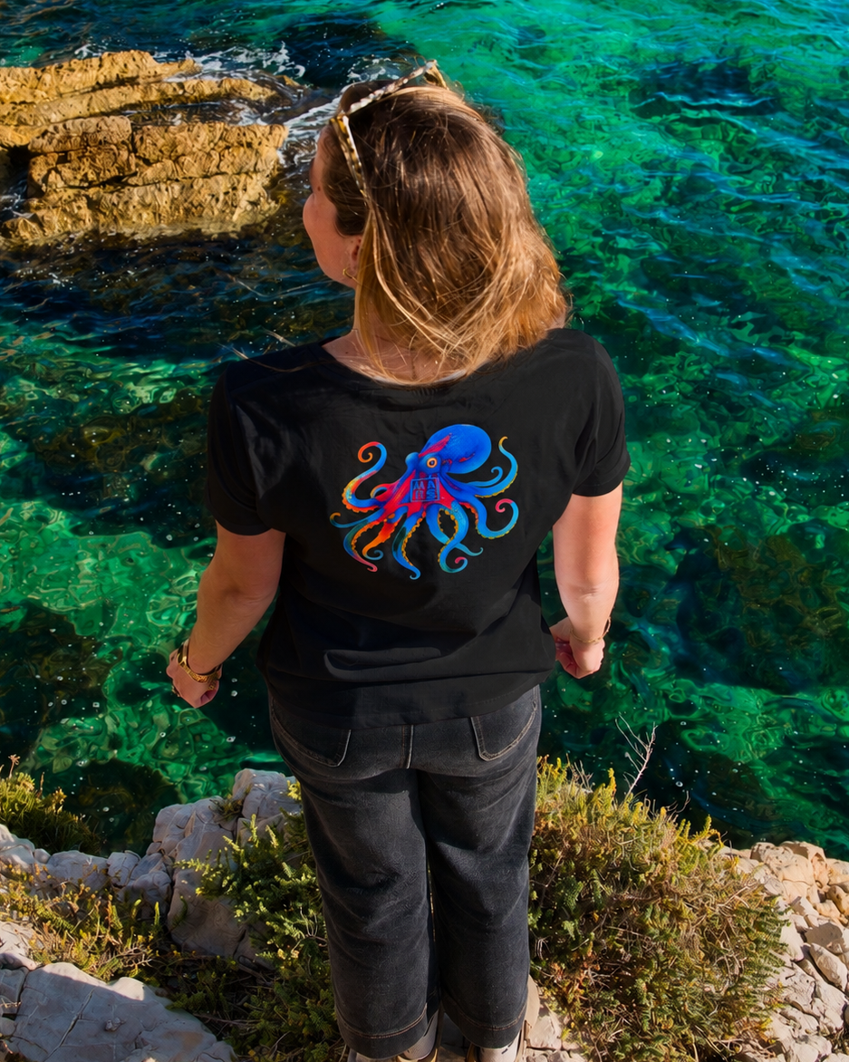 Une femme au bord de mer portant un t-shirt noir avec un dessin de poulpe