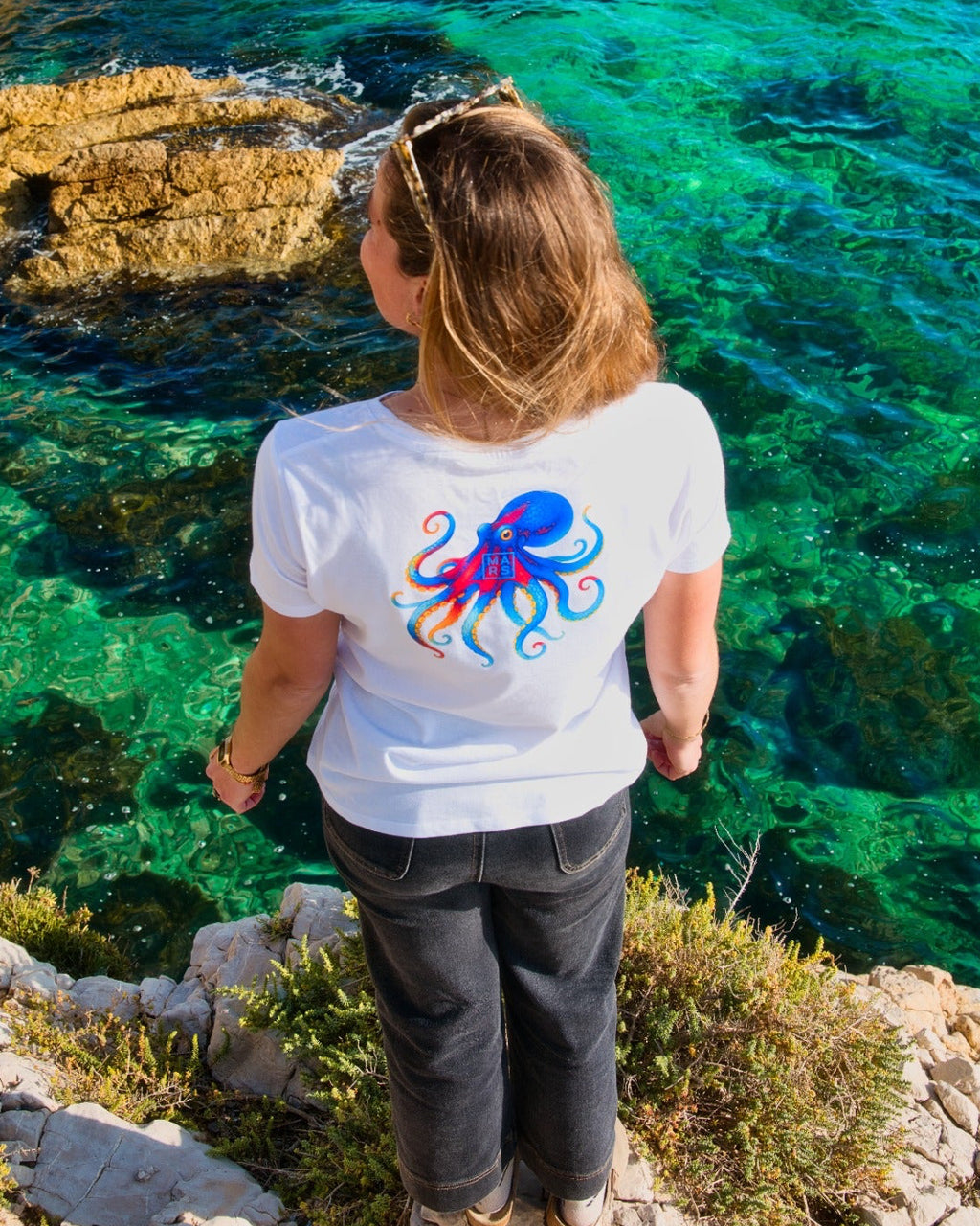 Une femme au bord de mer portant un t-shirt blanc avec un dessin de poulpe