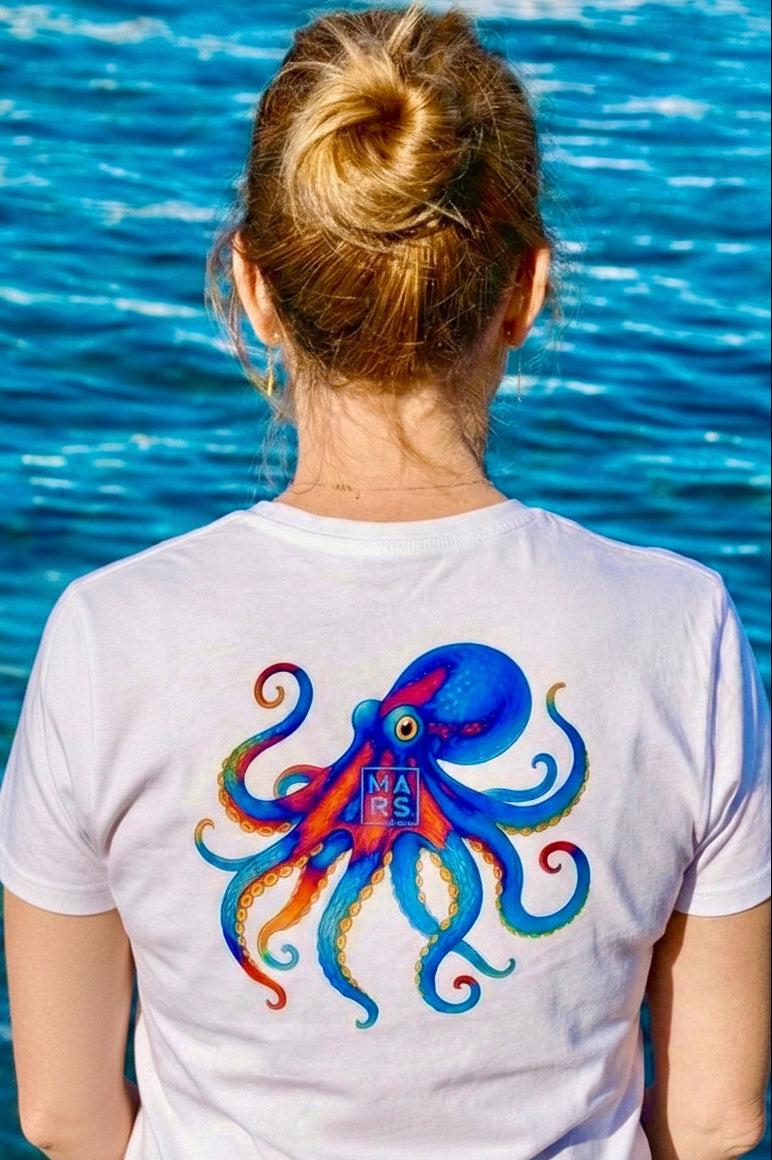 Une femme au bord de mer avec un T-Shirt blanc et une illustration de poulpe sur le dos